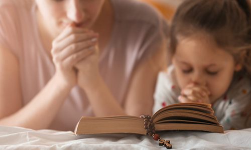 A mother and child living the Christian lifestyle, praying with the Bible for divine guidance and blessings.