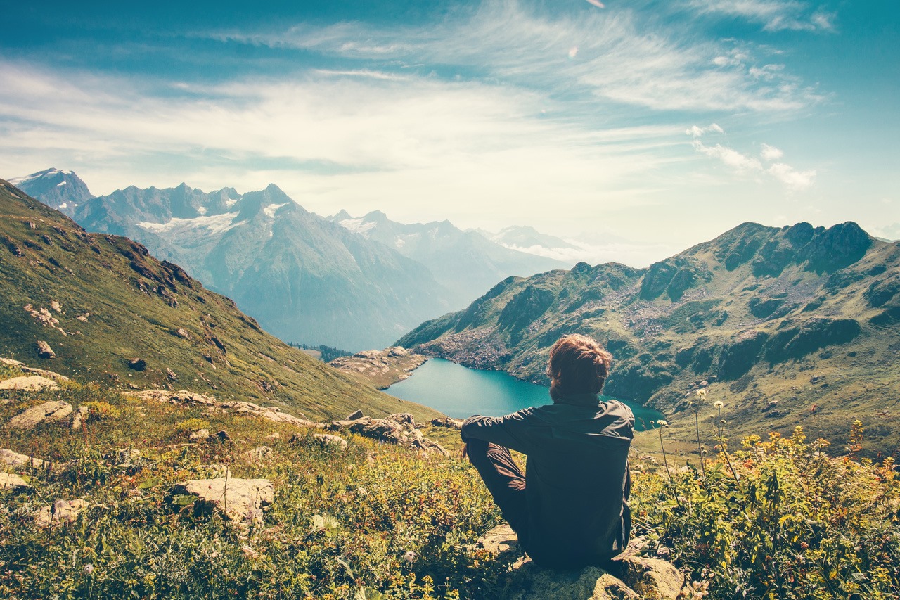 The man is seated, facing the mountain lake, reflecting on the Christian lifestyle.